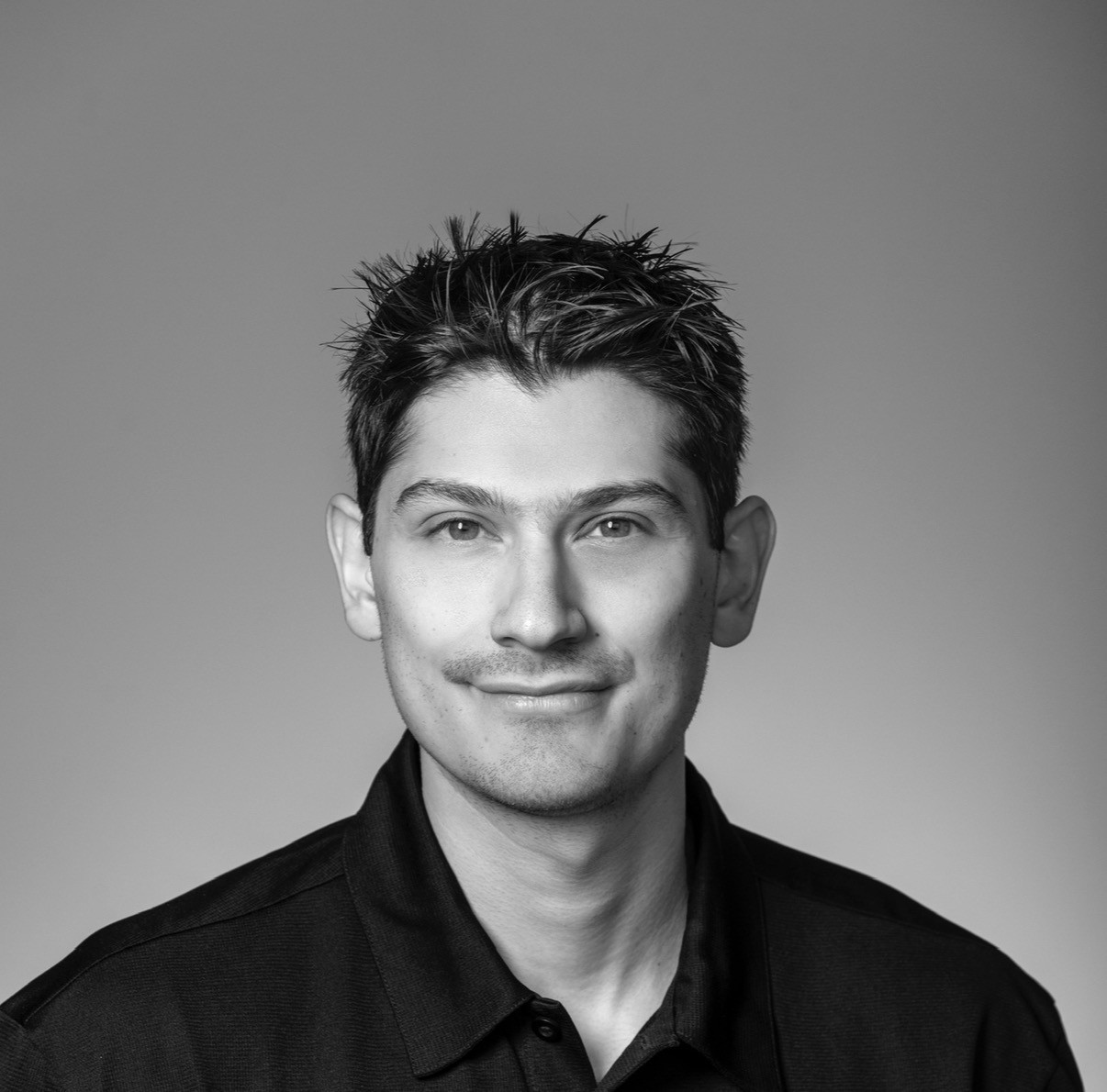 Black and white portrait of a dance instructor posing in front of a dark background.
